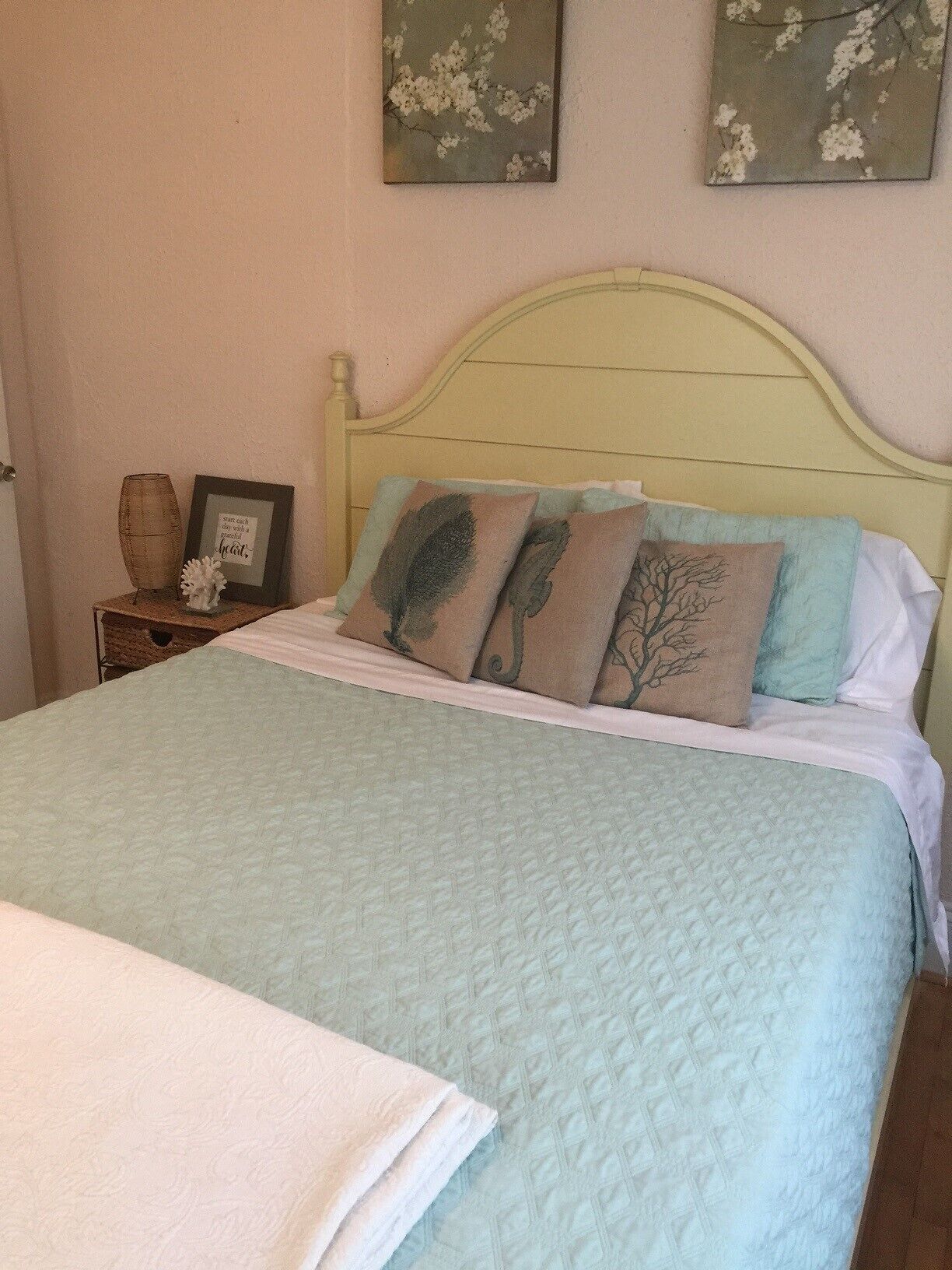 Una cama bien hecha con colcha acolchada, una manta blanca y varias almohadas con diseños de árboles.