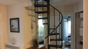 Una scala a chiocciola in una stanza con termosifone, un quadro appeso al muro e una pianta su una panca di legno.