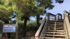 Una scala di legno che conduce a un cartello per l'accesso alla spiaggia, con una veduta costiera.
