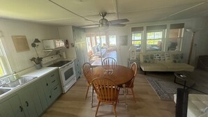 A kitchen with wooden cabinets, a dining table with chairs, a ceiling fan, and a view of a patio area. - Port Bay Waterfront Cottage — Your Private Lakeside Escape (Wolcott)