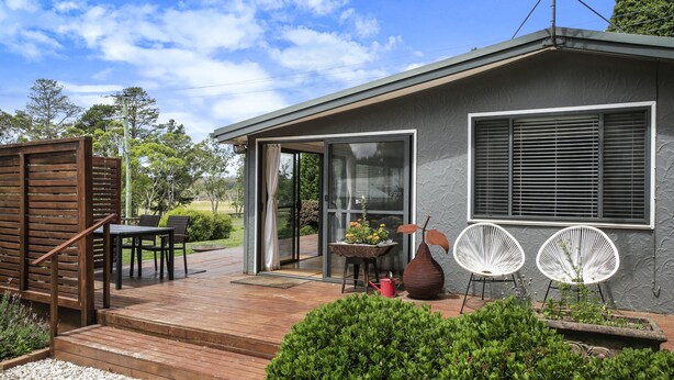 A modern house with a wooden deck, a dining area with chairs, a potted plant, and two white chairs outside. - Twin Oaks Cottage - Fitzroy Falls  (Fitzroy Falls)
