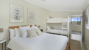 A bedroom with a large bed, a lower bunk bed, and two framed pictures on the wall. - Twin Oaks Cottage - Fitzroy Falls  (Fitzroy Falls)