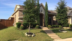 A residential house with a brick facade, a stone archway entrance, and a well-maintained lawn with young trees and a stone pathway leading to the front door. - Joe Pool Lake Resort Style-Upscale Gorgeous Home!!! (Grand Prairie)