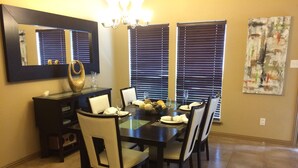 A dining room with a rectangular table set for four, flanked by two windows with blinds, a chandelier, and a large mirror above the table. - Joe Pool Lake Resort Style-Upscale Gorgeous Home!!! (Grand Prairie)