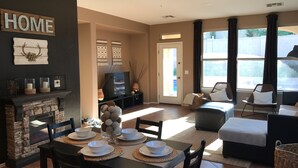 A living room with a fireplace, a television, and a dining area with a table set for four. - Goodyear Private Outdoor Pool Baseball Golf WIFI Parks Hike Nascar (Goodyear)