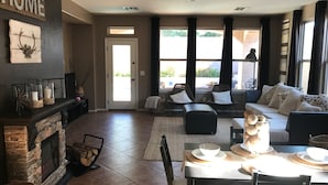 A spacious living room with a fireplace, a dining area with a table set for four, and a comfortable seating area with a sofa and chairs. - Goodyear Private Outdoor Pool Baseball Golf WIFI Parks Hike Nascar (Goodyear)