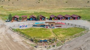 Un camping con varias cabañas, un espacio común con juegos para niños y un área de estacionamiento cercada.