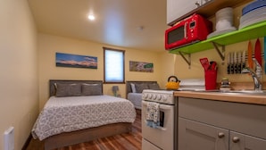 Una habitación pequeña con cama, kitchenette y ventana.