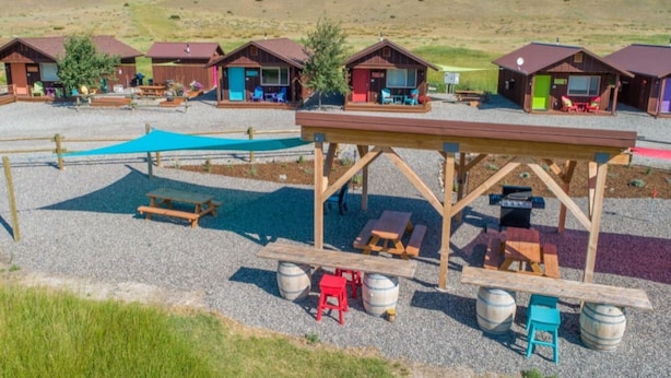 Un camping con cabañas de madera, mesas de picnic y parrillas.