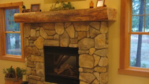 A stone fireplace with a log fire, flanked by windows with a view of trees. - Wonderful Winter Escape with Mountain views in Forest-like setting (Burney)