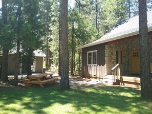 Una cabaña con fachada de piedra, terraza de madera y mesa de picnic.