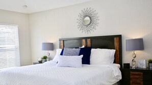 Un dormitorio ordenado con una cama grande, dos lámparas de noche, un espejo decorativo y una mesita de noche con una planta.