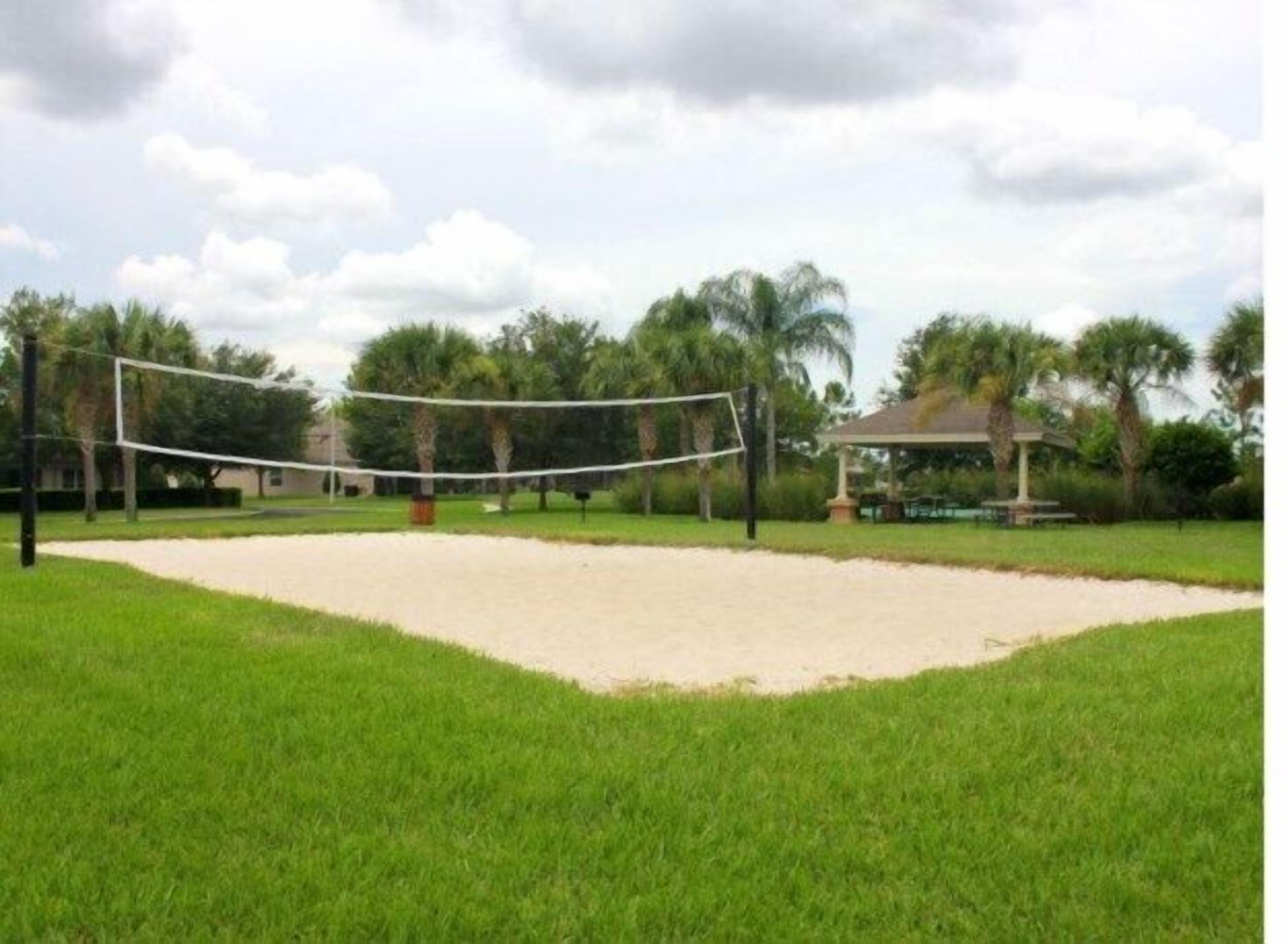 Una cancha de voleibol con red, rodeada de césped y palmeras.