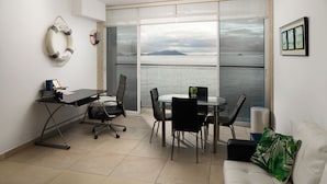 Ein modernes Zimmer mit Schreibtisch, Stühlen, einer Couch und einem großen Fenster mit Blick aufs Meer.