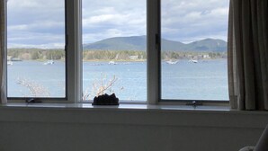 Een kamer met een groot raam dat uitkijkt op een wateroppervlak met boten en bergen in de verte.