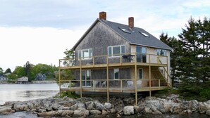 Een huis met twee verdiepingen en een balkon, gelegen aan een rotsachtige kustlijn met uitzicht op het water.