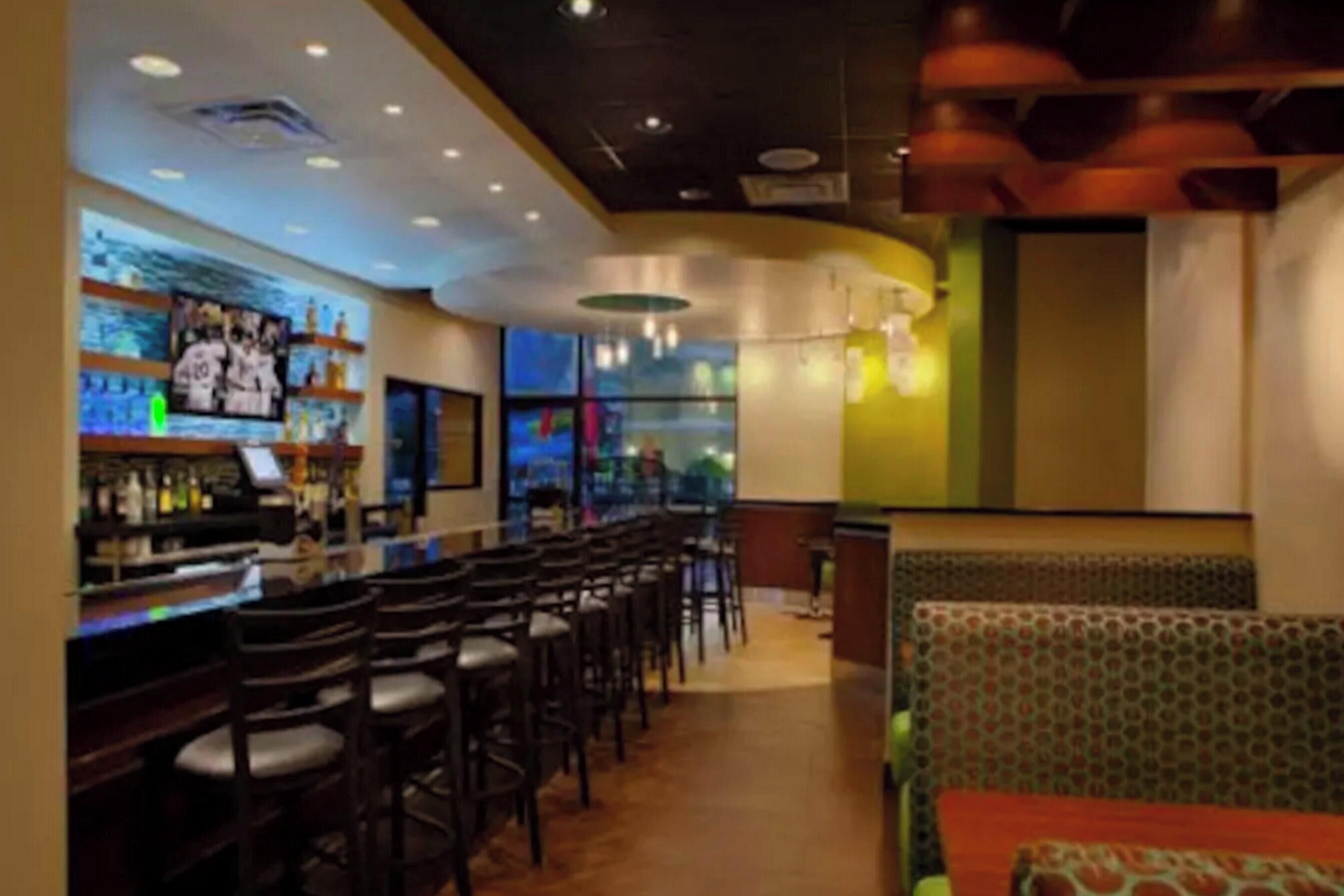 A bar area with multiple seating options, including bar stools and patterned booths, and a bar counter with various bottles.