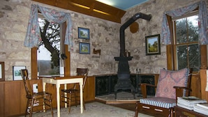 A rustic room with a stone wall, wooden furniture, a fireplace, and framed pictures.