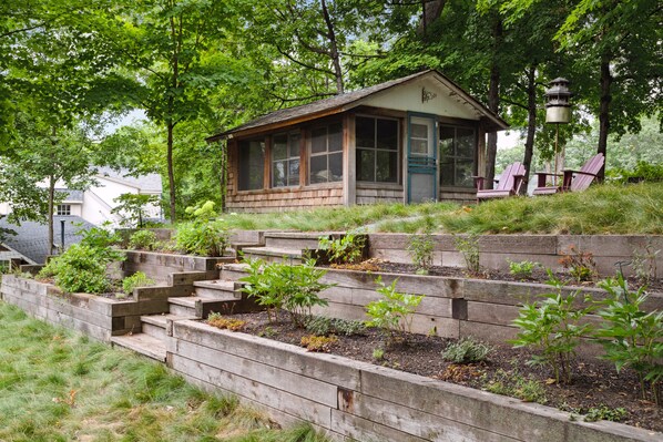 A rustic cabin with a porch, surrounded by a garden and wooden steps.
