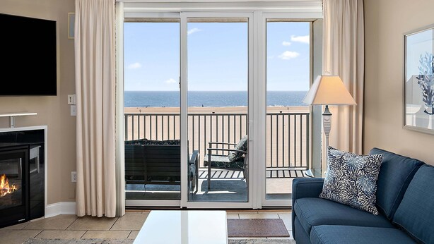 Ein Wohnzimmer mit Kamin, einer Couch, einem Fernseher und einem Balkon mit Meerblick.