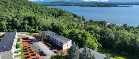 A multi-story building with a parking lot and a view of a lake and mountains.
