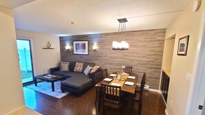 Una sala moderna con un sofá seccional gris oscuro, una mesa de comedor de madera y una lámpara de araña.