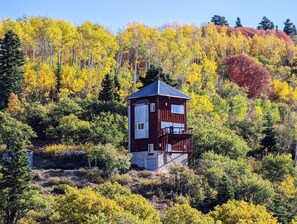 Eine Hütte mit roter Fassade, einem Balkon und Blick auf einen mit Herbstlaub bedeckten Wald.