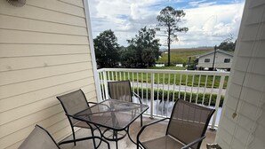 A covered patio with a table and four chairs, overlooking a grassy area and a body of water.
