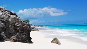 A beach with white sand, clear turquoise water, and rocky outcrops. - "The Cut Pearl" - Stunning Private Beachfront/Oceanfront Villa On Little Exuma (Forbes Hill)