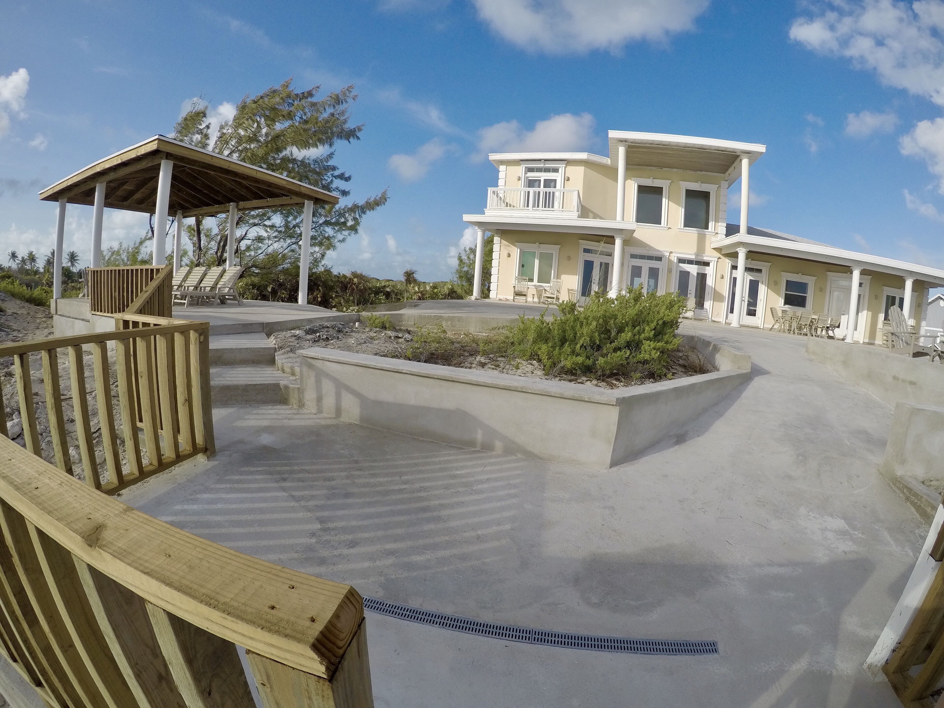 Una propiedad frente a la playa con un patio cubierto, piscina y un edificio de dos pisos con balcones.