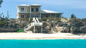 A two-story beachfront house with a balcony and a staircase leading to a beach area. - "The Cut Pearl" - Stunning Private Beachfront/Oceanfront Villa On Little Exuma (Forbes Hill)