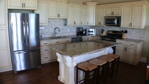 A kitchen with white cabinets, stainless steel appliances, a granite countertop, and a central island with stools. - "The Cut Pearl" - Stunning Private Beachfront/Oceanfront Villa On Little Exuma (Forbes Hill)