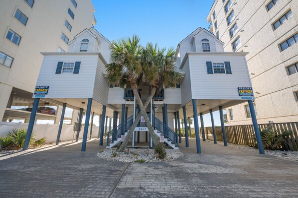 A hotel with a central staircase flanked by two buildings, each with a balcony and a palm tree.