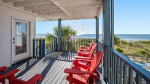 Una terraza techada con sillas Adirondack rojas y vista al océano.
