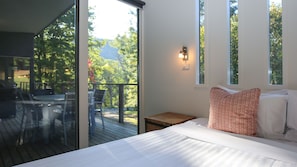 Relax in this serene bedroom with a large bed, a bedside table, and a nightstand, offering a view of the surrounding trees from the large window.