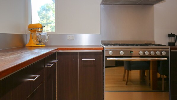 A kitchen with dark wooden cabinets, a stainless steel stove, and a yellow mixer.