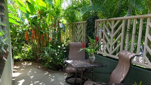 Een terras met een tafel en twee stoelen, omringd door weelderige begroeiing en een houten hek.