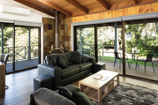 A modern living room with a wooden ceiling, a stone fireplace, a green sofa, and a wooden coffee table. - BEAUTIFUL COSY FAMILY HIDEAWAY - FREE WIFI AND FOXTEL/STAN - AMAZING LONG JETTY (Port Welshpool)
