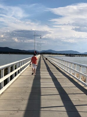 A long, straight pedestrian bridge with white railings, leading to a body of water and distant mountains. - BEAUTIFUL COSY FAMILY HIDEAWAY - FREE WIFI AND FOXTEL/STAN - AMAZING LONG JETTY (Port Welshpool)