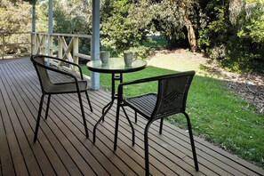 A wooden deck with two wicker chairs and a small round table, surrounded by greenery and trees. - BEAUTIFUL COSY FAMILY HIDEAWAY - FREE WIFI AND FOXTEL/STAN - AMAZING LONG JETTY (Port Welshpool)
