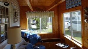 L’intérieur d’un chalet accueillant, avec un plafond en bois, une grande fenêtre donnant sur l’extérieur, un fauteuil bleu et une lampe.