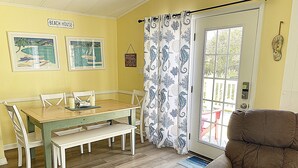 Uma área de jantar com uma mesa e cadeiras de madeira, uma poltrona marrom e uma porta com cortina em formato de cavalo-marinho.