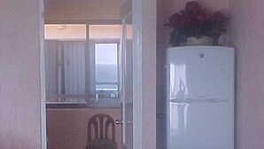 A compact kitchen with a refrigerator, a dining table, and a chair. -    Quality Cancun Condo Rental Within Your Vacation Budget?                      (Cancún)