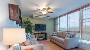 A living room with a ceiling fan, air conditioning unit, a flat-screen TV, a sofa, a coffee table, and a lamp. - Spacious Garden Retreat at Vistamar Combate, WiFi, full A/C, walk to the beach (Cabo Rojo)