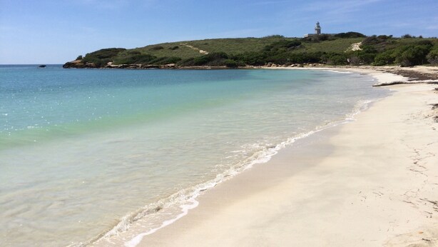 A beach with clear water, sandy shore, and a hill with a lighthouse. - Spacious Garden Retreat at Vistamar Combate, WiFi, full A/C, walk to the beach (Cabo Rojo)