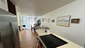 A kitchen with a stainless steel refrigerator, a black stove, and a tiled floor. There is a dining area with a table and chairs, and a plant on the counter. - Spacious Garden Retreat at Vistamar Combate, WiFi, full A/C, walk to the beach (Cabo Rojo)
