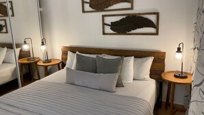 A neatly made bed with a wooden headboard, two bedside tables with lamps, and two wall-mounted leaf decorations. - Spacious Garden Retreat at Vistamar Combate, WiFi, full A/C, walk to the beach (Cabo Rojo)
