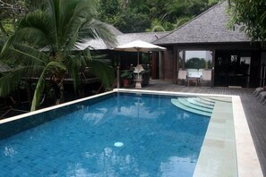 Relax by the pool surrounded by a wooden deck and lush palm trees.