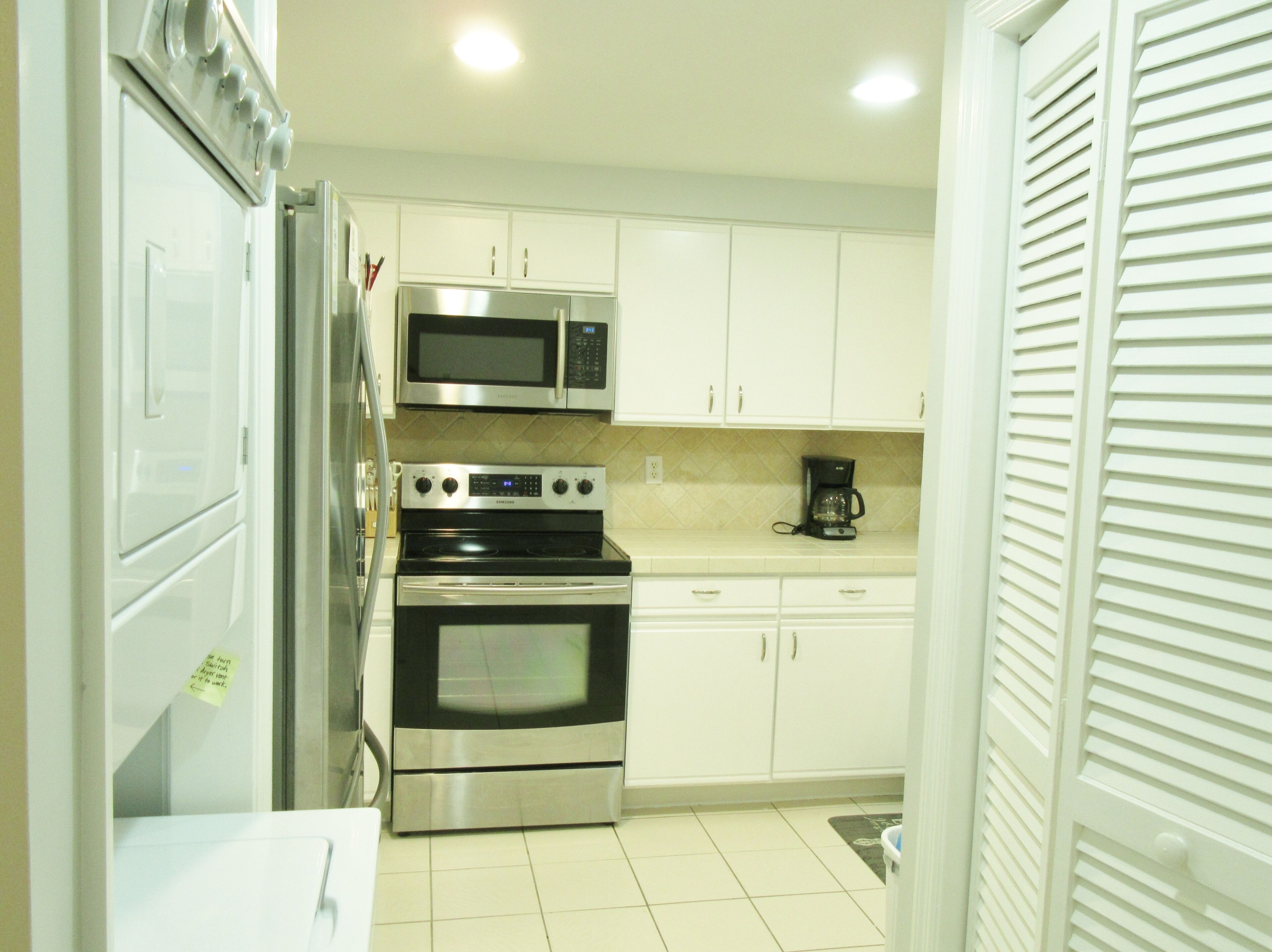 Cocina compacta con gabinetes blancos, refrigerador de acero inoxidable, microondas, estufa y cafetera.