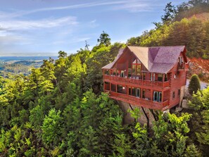 A red log cabin with multiple balconies, surrounded by dense forest and overlooking a valley. - High On The View: Spectacular View, Resort Pool, Deluxe, Top Amenities, near all Area Attractions! (Sevierville)